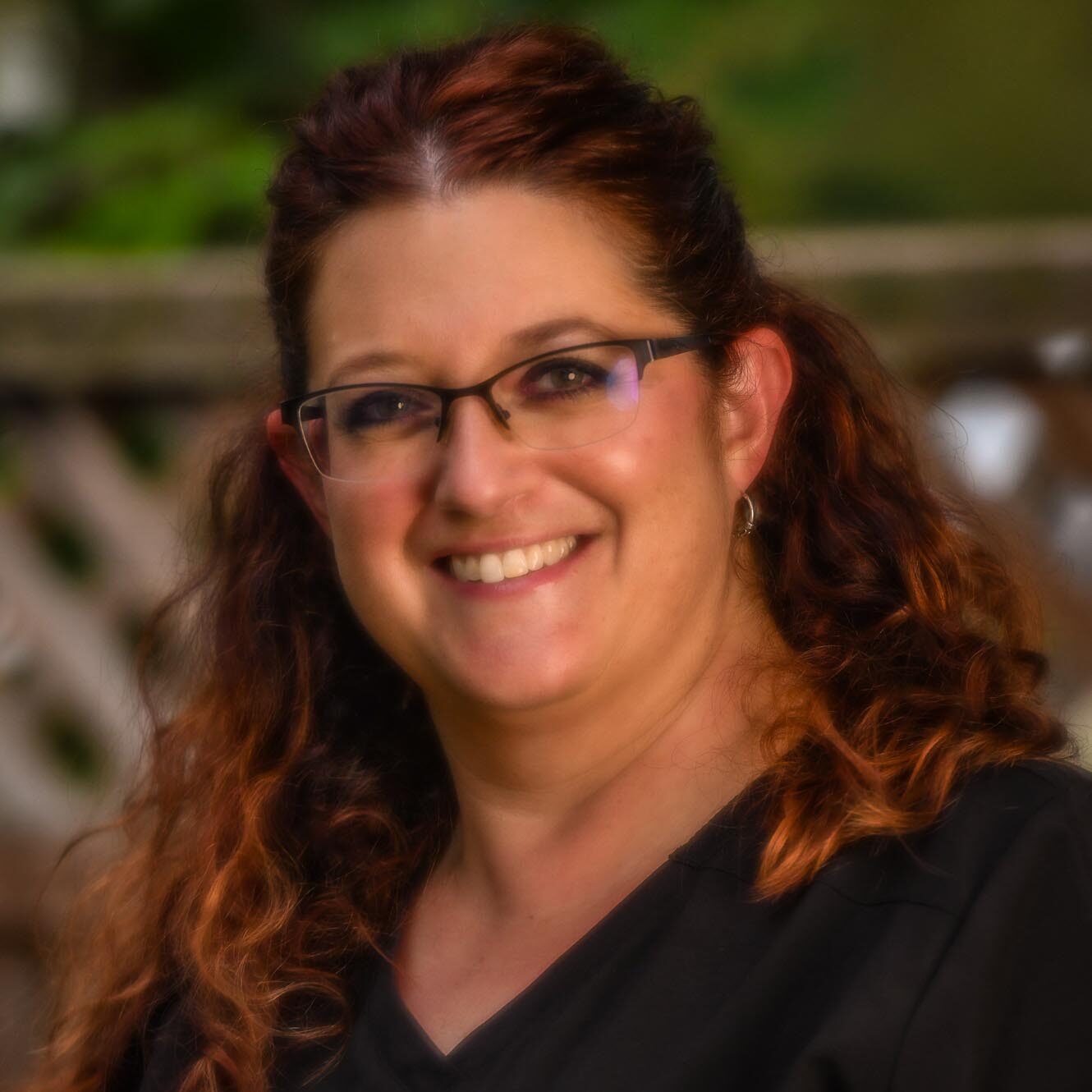 A woman with red hair and glasses smiling, radiating warmth and happiness. She is Lori, Dental Hygienist at Clinton Family Dental.